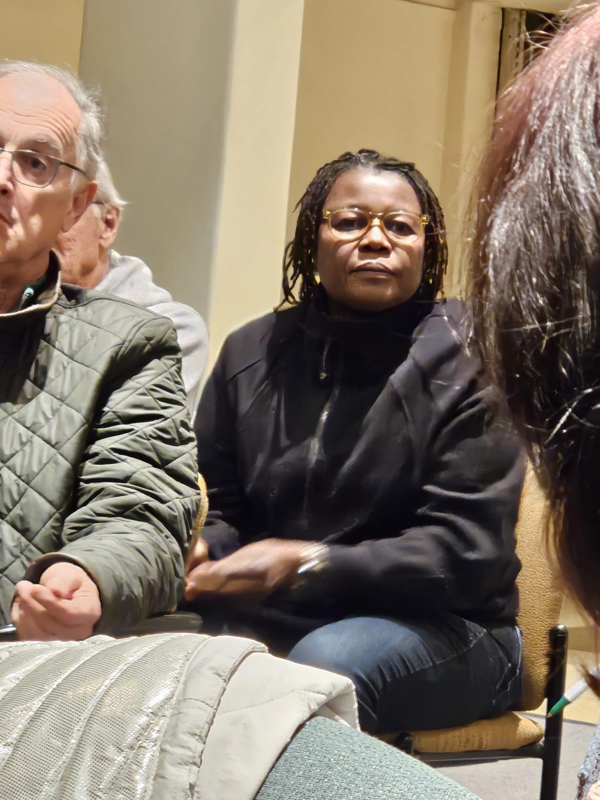 20250319_190517 (2) African-American woman with glasses in black top and jacket listening to reactions to what she just said